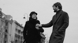 A black and white photo of a couple holding hands while walking along a sidewalk